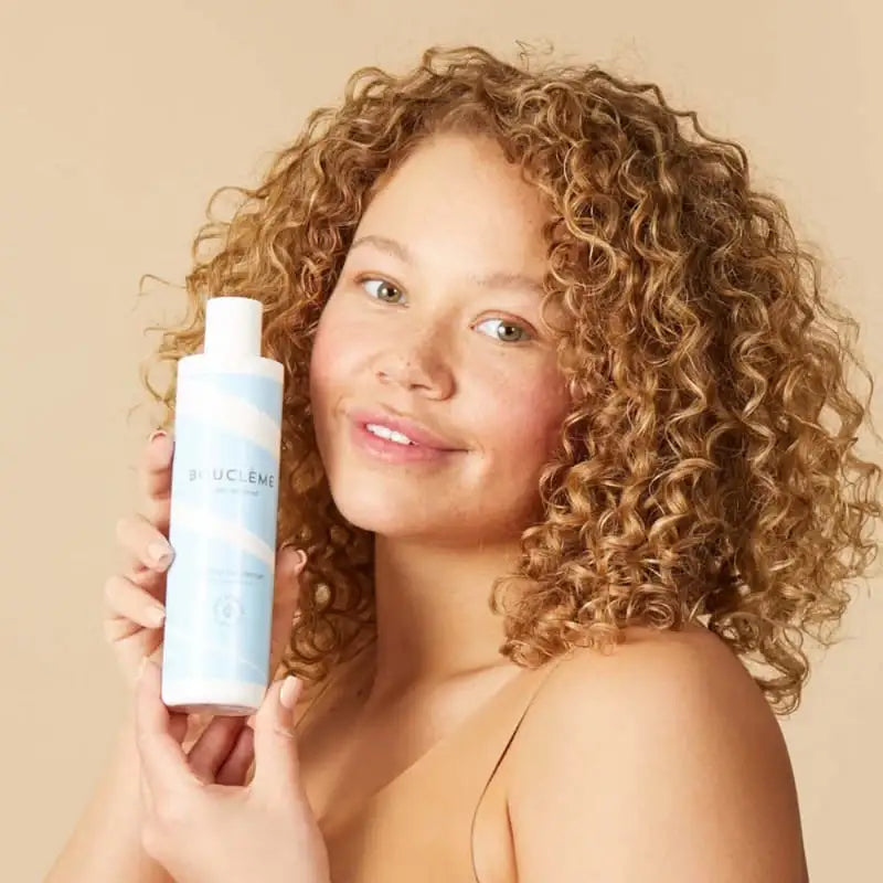Woman with curly hair holding Bouclème curl care product for defined, healthy curls