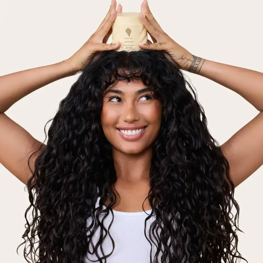 Woman with voluminous curly hair holding a curl care product, showcasing natural texture and shine.