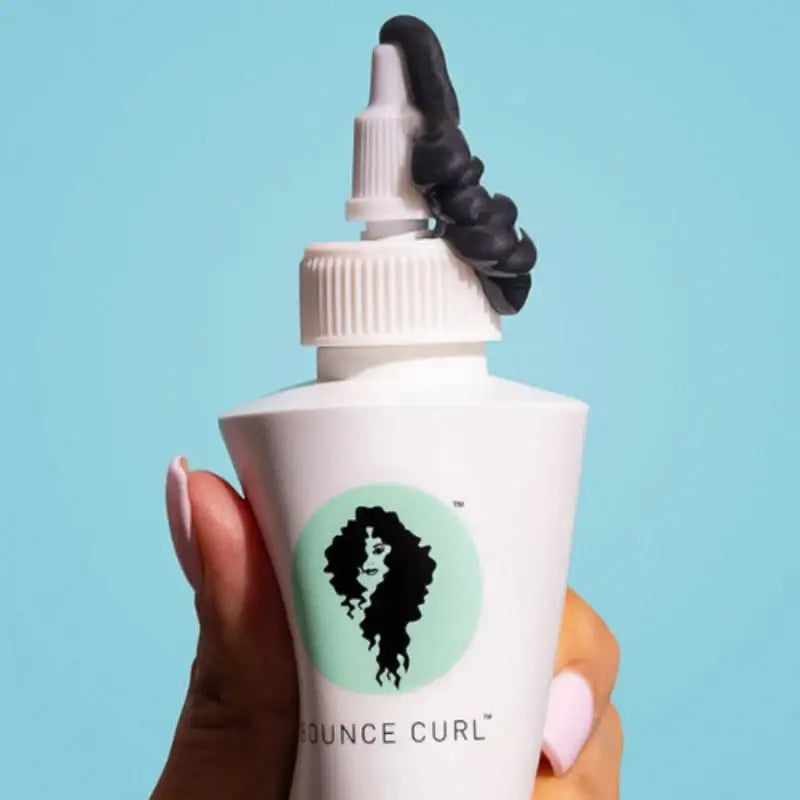 Bounce Curl product with defined curls on bottle, held against blue background for curly hair care