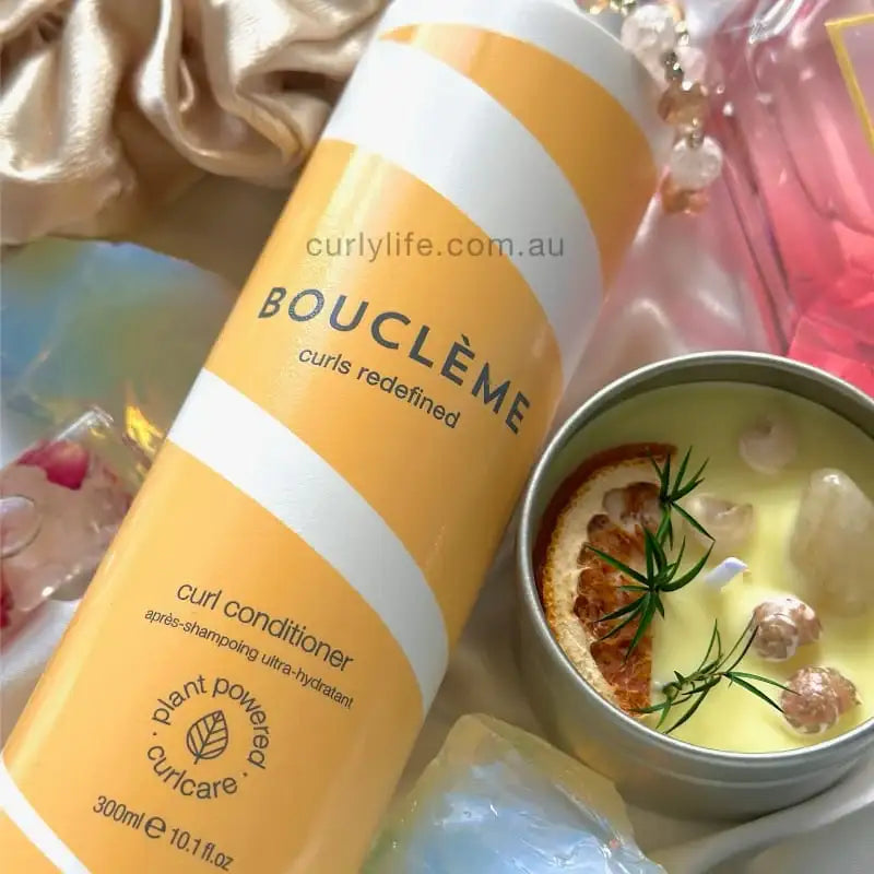 Bouclème curl conditioner bottle with plant-powered formula, styled beside a decorative candle and silk fabric