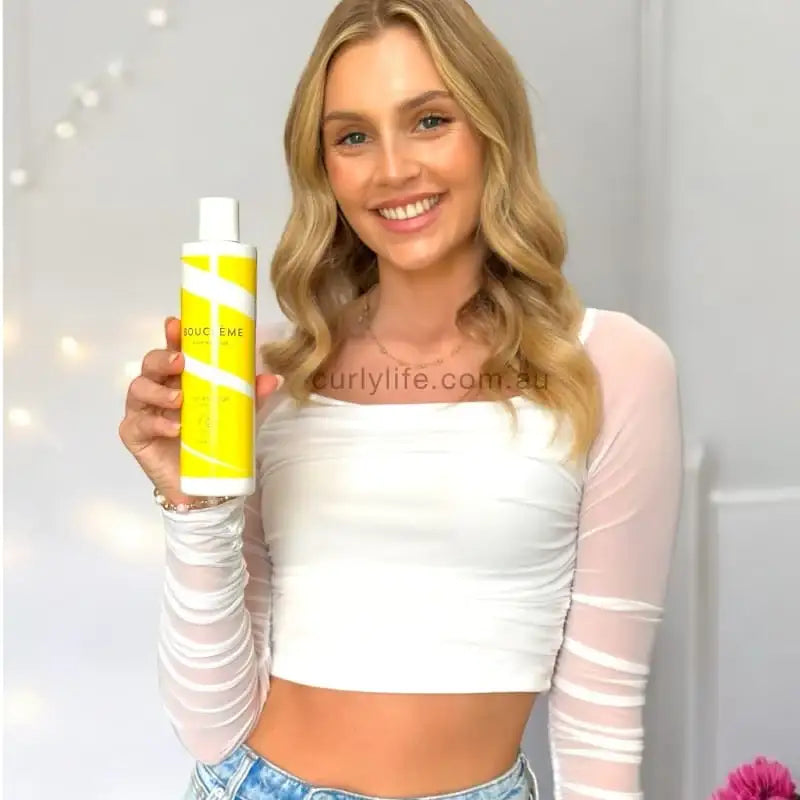 Woman holding yellow curly hair product, showcasing wavy locks and stylish white top.