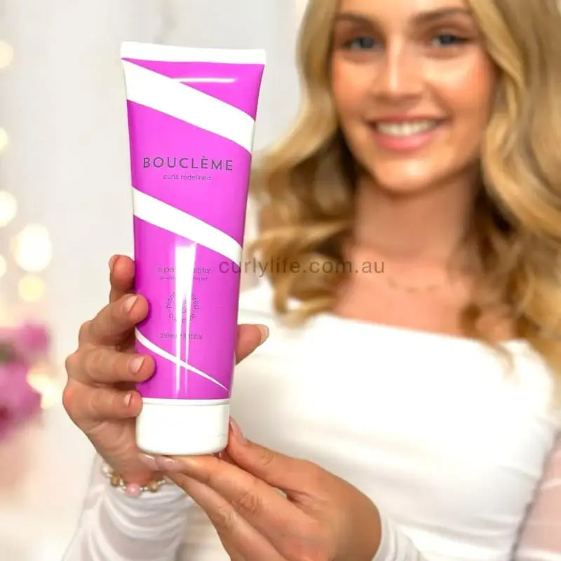 Bouclème Super Styler for curly hair, held by smiling woman with wavy locks, perfect for curl definition and care.