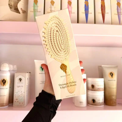 Bounce Curl Detangle Define EdgeLift Brush for curly hair care, held in hand with product shelves in background